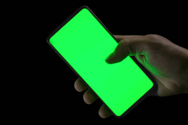 istock Isolated human hand holding a green screen smartphone on black background,hi tech addiction concept 1311850321