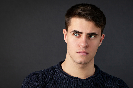 Close up studio portrait of 19 year old man with short brown hair in blue sweater on black background