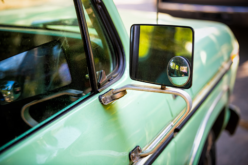 Closeup of green vintage retro style small car parked in Charleston, SC with reflection on side rear view mirror glass