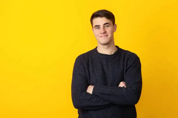 Studio portrait of 19 year old man with short brown hair in blue sweater on yellow background