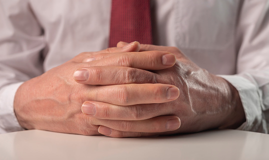 Businessman hands clasped, interlocked or folded close up on desk.