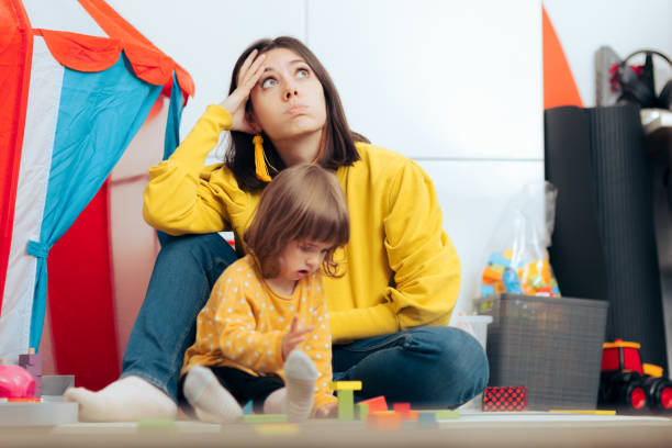 Tired Bored Mother Watching her Daughter Playing at Home Exhausted overwhelmed mom thinking concerned being stressed and wondering about daily problems worried mom with kids stock pictures, royalty-free photos & images