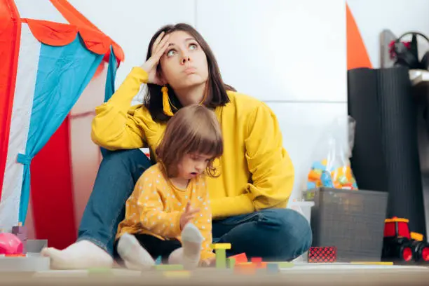 Photo of Tired Bored Mother Watching her Daughter Playing at Home