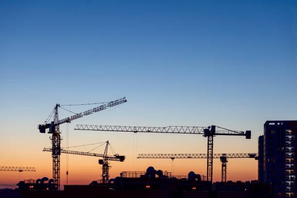 Silhouettes of tower cranes at sunset on the construction site