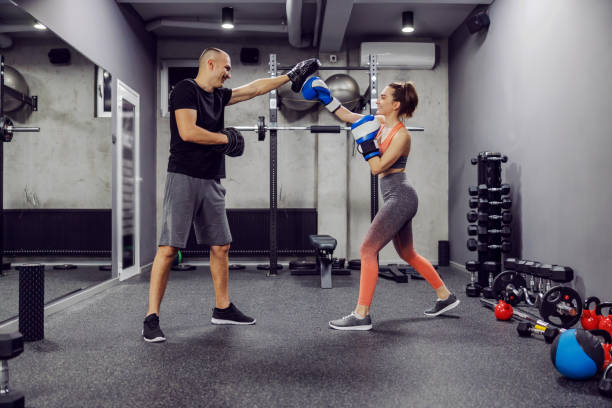 Boxing training class. The girl wears boxing gloves and hits the protection worn by the trainer at the gym. Using boxing mitts with a partner. Mobility and body strength in boxing functional training Boxing training class. The girl wears boxing gloves and hits the protection worn by the trainer at the gym. Using boxing mitts with a partner. Mobility and body strength in boxing functional training weight class stock pictures, royalty-free photos & images