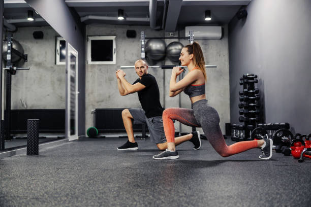 ejercer un paso adelante, el concepto de entrenamiento personal para dos. un hombre de fitness y una mujer hacen ejercicios deportivos para calentar y quemar los músculos de las piernas. objetivo de aptitud de la relación - stretching boyfriend indoors lifestyles fotografías e imágenes de stock