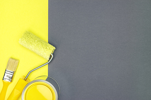 paint roller, paintbrush and can with yellow paint on yellow and gray background. home renovation tools. flat lay.