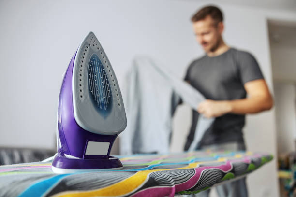 Photo frame of an Isolated laundry iron with a metal warming plate on the ironing board on the background copy space. A man who does housework, a good husband, or a single man. Modern lifestyle Photo frame of an Isolated laundry iron with a metal warming plate on the ironing board on the background copy space. A man who does housework, a good husband, or a single man. Modern lifestyle laundry husband housework men stock pictures, royalty-free photos & images