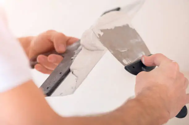 A man with two spatulas in his hands applies putty, very close-up selective focus