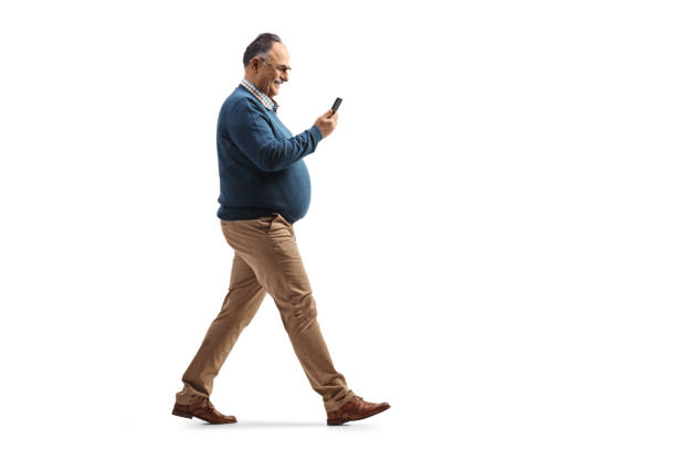 Full length profile shot of a mature man using a smartphone and walking Full length profile shot of a mature man using a smartphone and walking isolated on white background chubby arab stock pictures, royalty-free photos & images