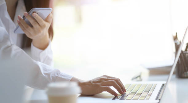 istock Cropped image of female holding smartphone getting message with confirmation making transaction on laptop computer,woman using mobile phone app for synchronizing data with netbook via bluetooth. 1311925424