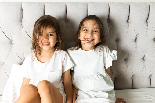 Two cute little girls laughing having fun together looking at camera in bedroom.