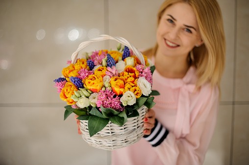 elegant white wicker basket with flower arrangement of fresh tulips, roses, muscari and hyacinths in the woman's hands
