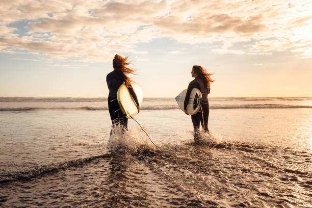 widok z tyłu dwóch pięknych młodych kobiet z deską surfingową. - murawai beach zdjęcia i obrazy z banku zdjęć