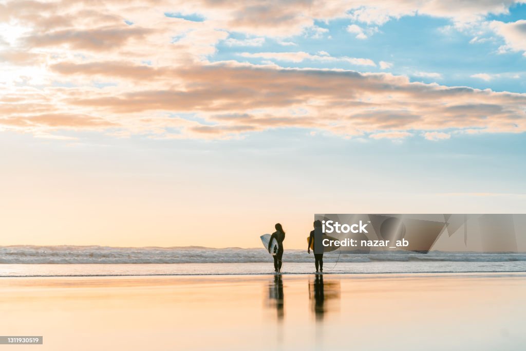 We can do it. Two young woman surfing on beach with surfboard at sunset time. Beach Stock Photo