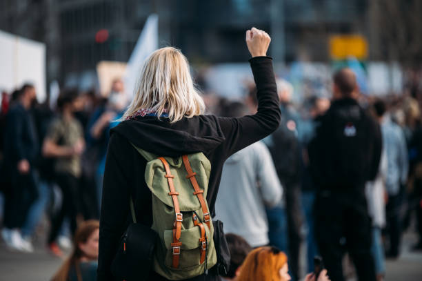 rear view of a female protester raising her fist up - youth organization imagens e fotografias de stock