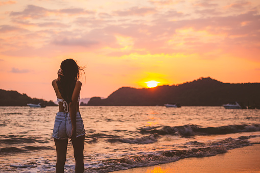 Summer travel vacation concept, Happy traveler asian woman with white bikini and shorts jeans relax and walk on sea beach in sunset at Koh Mak, Thailand