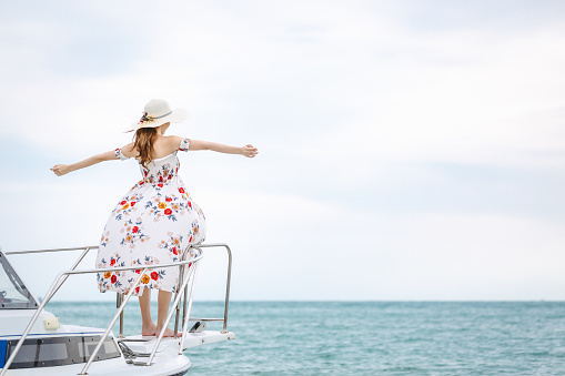 Travel summer vacation concept, Happy solo traveler asian woman with dress and hat relax on sailboat in tropical sea at Pattaya, Thailand