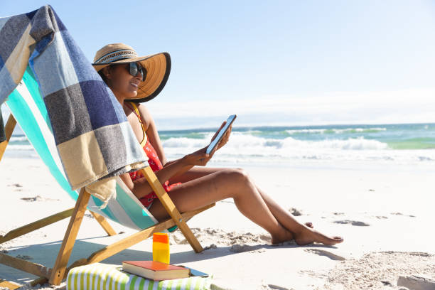 istock Mixed race smiling woman on beach holiday sitting in deckchair using tablet 1311932709