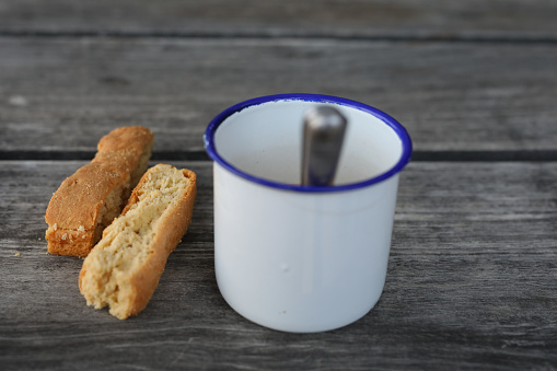 A close up of rusks next to a cup of coffee. The coffee is in a metal cup and is on a wooeden table