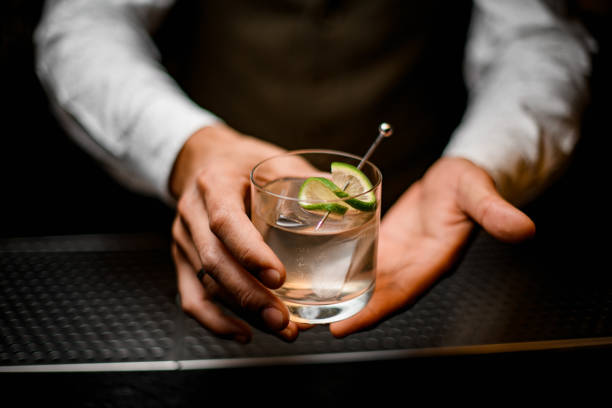 close-up on hands of man bartender holding glass with cold drink beautiful close-up on hands of man bartender holding glass with cold drink with ice cube decorated with lime bartender stock pictures, royalty-free photos & images