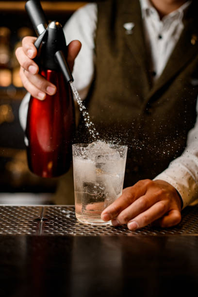barista uomo aggiunge acqua gassata dal sifone al bicchiere di cristallo con bevanda - siphon foto e immagini stock