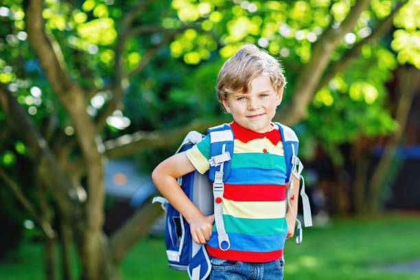 happy little kid boy in colorful shirt and backpack or satchel on his first day to school or nursery. child outdoors on warm sunny day, back to school concept. boy in colorful uniform - little boys preschooler back to school backpack imagens e fotografias de stock