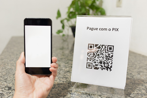 QR Code facilitating payments and electronic money transfers. Closeup of a hand holding a smartphone with the blank screen to be able to write. PIX is a new electronic payment method in Brazil.