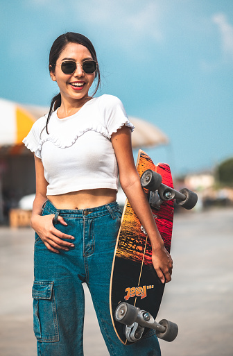 Asian young women surf skate or skates board outdoors on beautiful summer day. Happy young women happy play surf skate  at rooftop city bangkok.