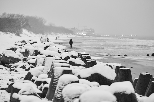 Concrete breakwaters covered with snow against background of winter sea. Coastal protection in snow. Snowy cloudy seascape.