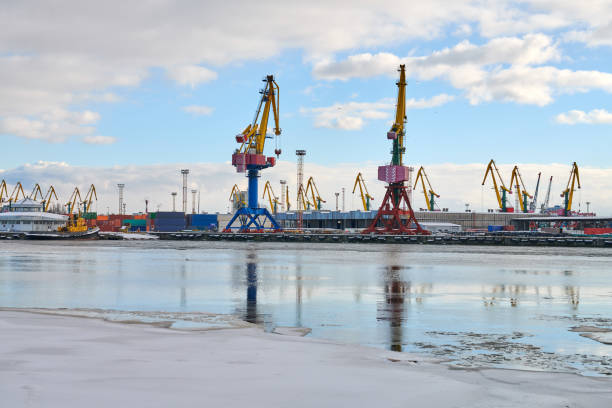 Moored cargo ships and harbor cranes in port. Seaport, cargo container yard, container ship terminal, shipyard. Business and commerce, logistics. Winter industrial scene.