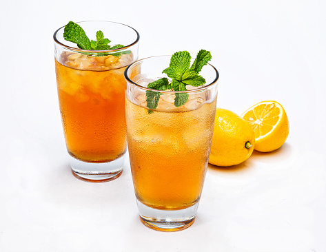 Two glasses of ice tea with mint, on a white background with lemons