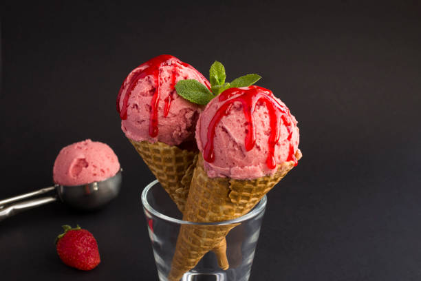 istock Close-up on strawberry ice cream in a waffle cone on the black background. Copy space. 1311956332