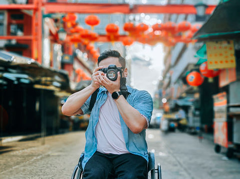 asian chinese male with physical disability on wheelchair photographing in china town sitting on his wheelchair