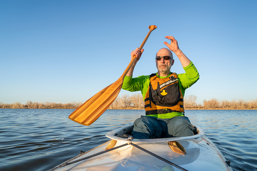 senior male is paddling expedition canoe, early spring scenery on a lake in northern Colorado, POV from boat bow