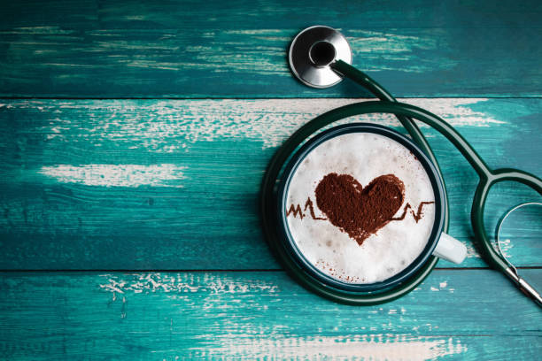 World Health Day. Health Care for Coffee Lover and Heart Disease Concept. Latte Art by Cinnamon on Top as Heart Shape and Pulse Beat Rate. Hot Coffee Cup Lay on Table inside Stethoscope. Top View día mundial de la salud. concepto de cuidado de la salud para el amante del café y las enfermedades cardíacas. arte de café con leche por canela en la parte superior como forma del corazón y ritmo de pulso. taza de café caliente yacía en la mesa den
