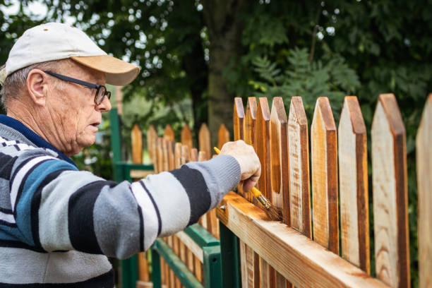 Senior man paint picket fence with wood stain Active senior man painting wooden fence in garden. Old craftsman working at backyard. Repairing picket fence brush fence stock pictures, royalty-free photos & images