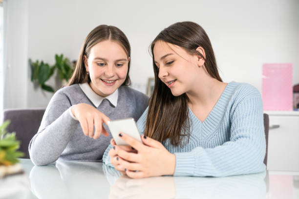 istock Beautiful young sisters looking at mobile cell phone having fun at home 1311965478