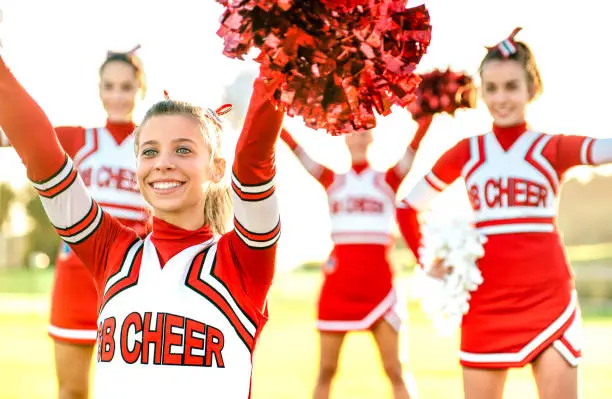 Group of female cheerleaders performing outdoors at university campus - Sport concept of cheerleading team training at high school during sunset - Warm backlight filter with focus on left girl eyes