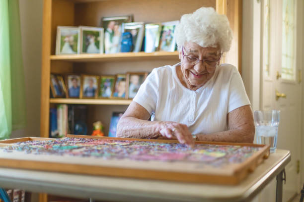 elderly woman at home working on jigsaw puzzle active senior photo series - jigsaw puzzle puzzle finishing white imagens e fotografias de stock