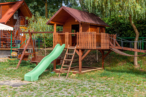 Empty modern wooden children playground set on green yard in public park in summer day. Funny toy land for kids. Urban exercise activities for child outdoors. Neighborhood childhood concept