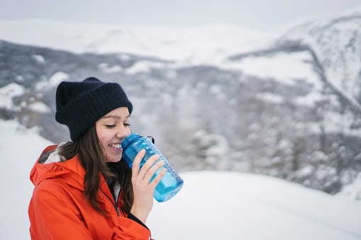 She drinks from water bottle, snowy Swiss Alps in the distance