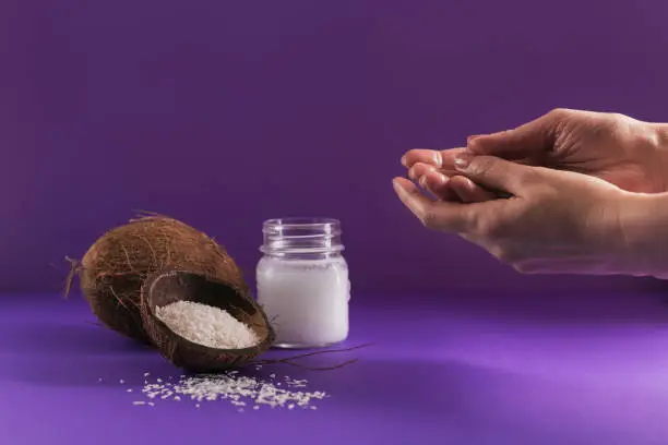 Composition with natural organic coconut oil cosmetic body cream on purple color background. Woman's hands with oil. Natural beauty and skincare concept