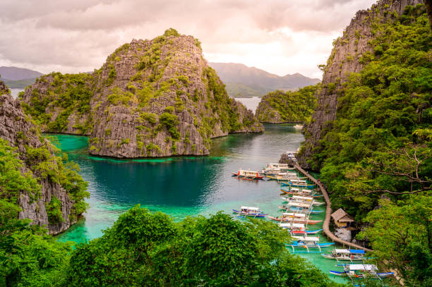 błękitna woda kryształowa w rajskiej zatoce z łodziami na drewnianym molo nad jeziorem kayangan na wyspie coron, palawan, filipiny. - kayangan lake zdjęcia i obrazy z banku zdjęć