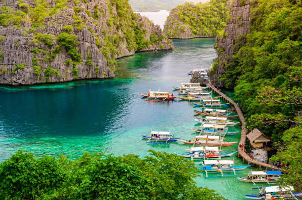 błękitna woda kryształowa w rajskiej zatoce z łodziami na drewnianym molo nad jeziorem kayangan na wyspie coron, palawan, filipiny. - kayangan lake zdjęcia i obrazy z banku zdjęć