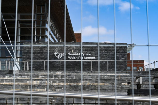 Welsh Parliament building blocked off by wire mesh fencing Cardiff Bay, Wales - April 2021: Sign on the wall of the Welsh Parliament building, The Senedd, seen behind wire mesh fencing. The barrier was erected to prevent crowds of young people gathering around the building at night. national assembly for wales stock pictures, royalty-free photos & images