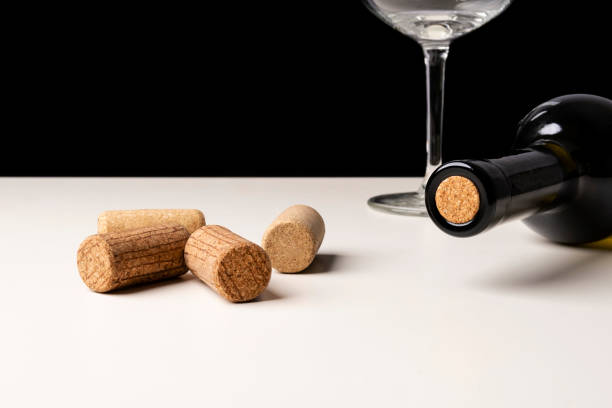 istock Bottle of white wine, wine glass and corks on white table against black background. Selective focus, minimalistic, vivid colors. 1311989771