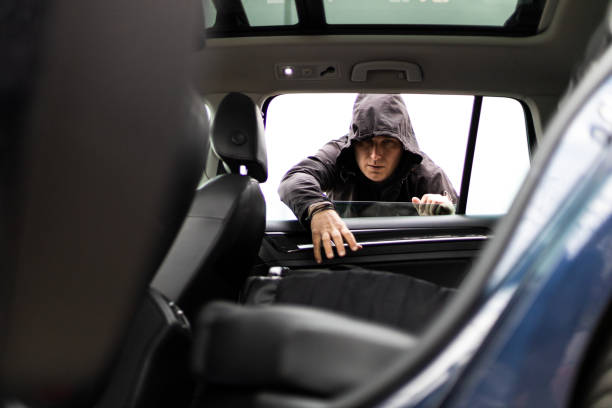 istock Hooded thief with mask stealing backpack from a parked car 1311991762