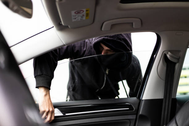 istock Hooded thief with mask stealing from a parked car 1311992547