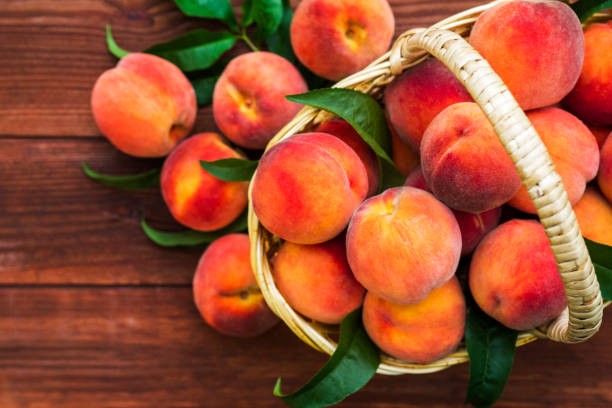 freshly picked peaches in basket on a brown wooden background. ripe peaches in basket on wooden table. - nectarine peach red market imagens e fotografias de stock